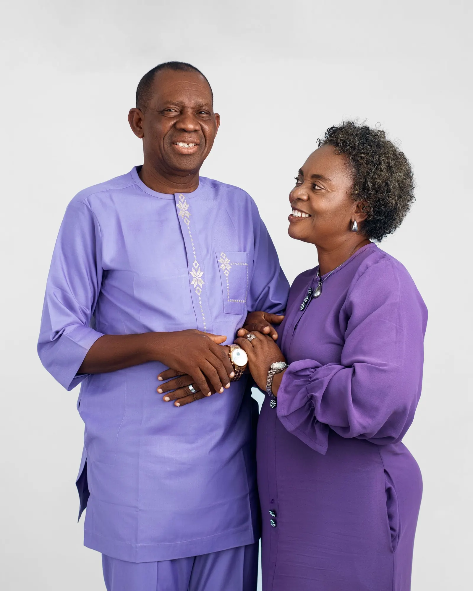 Smiling older Nigerian couple in matching purple outfits holding hands